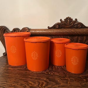 May include: Set of four orange canisters with a floral design. The canisters are made of plastic and have a vintage look.