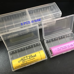 Puede incluir: Seis cajas de almacenamiento de baterías de plástico transparente con dos baterías recargables 18650 amarillas y una morada. Las cajas tienen una etiqueta que dice "All+Best 18650 Flat Top Rechargeable 3.7V 40A 3000mAh". Una batería tiene una etiqueta que dice "INR 18650-300P 3.7V KFALO 3000MAH 15A".