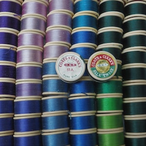 May include: A close-up of spools of Coats & Clark's O.N.T. silk thread in various colors, including purple, blue, green, and white. The spools are arranged in rows and feature the Coats & Clark's logo and branding.