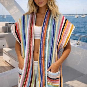 May include: A colorful striped beach cover-up with pockets. The cover-up is made of a soft, absorbent material and features vertical stripes in various colors. A straw hat with a brown band is also visible.