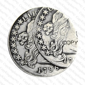 May include: A silver replica of a 1796 Liberty Dollar coin. The coin features a profile of Liberty with flowing hair and a ribbon tied around her head. The inscription "LIBERTY" is visible on the coin, along with the date "1796".
