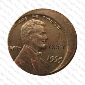 May include: A copper-colored 1955 United States penny coin with the words "In God We Trust" and "Liberty" visible. The coin features a profile of Abraham Lincoln on the obverse side.
