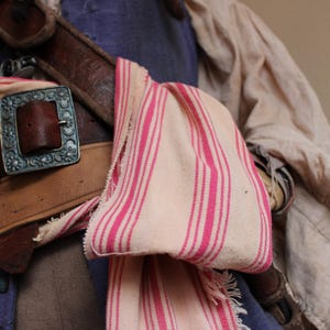 May include: A close-up of a brown leather belt with silver buckles and a white and pink striped fabric draped over it.