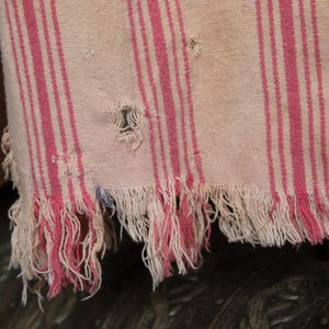 May include: A white and pink striped fabric with a frayed edge. The fabric has a worn and distressed look.