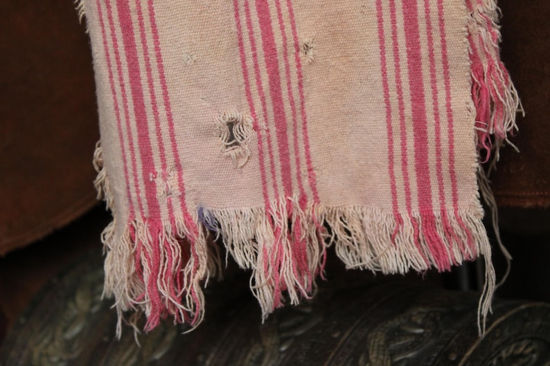May include: A white and pink striped fabric with a frayed edge. The fabric has a worn and distressed look.
