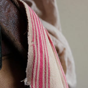 May include: A close-up of a brown leather belt with a metal buckle. The belt is worn and has a faded look. A white and pink striped fabric is draped over the belt.