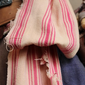 May include: A white and pink striped fabric with a frayed edge. The fabric is folded and draped over a brown leather belt.