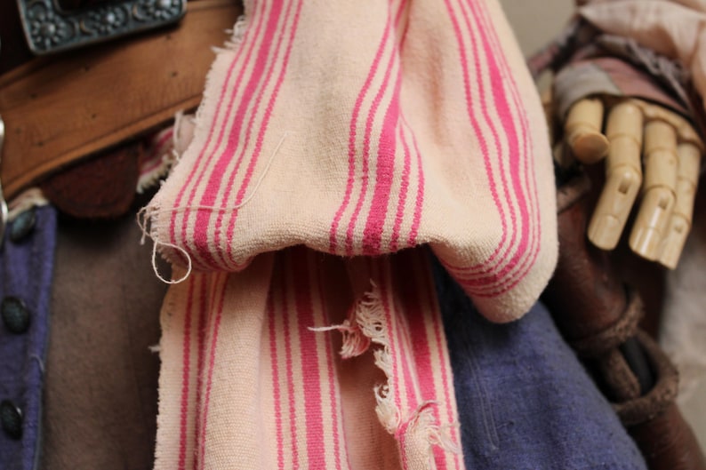 May include: A white and pink striped fabric with a frayed edge. The fabric is folded and draped over a brown leather belt.