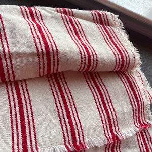 May include: White fabric with red stripes and a frayed edge. The fabric is folded in half.