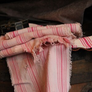 May include: A pink and white striped fabric with frayed edges. The fabric is folded and draped over a wooden surface.