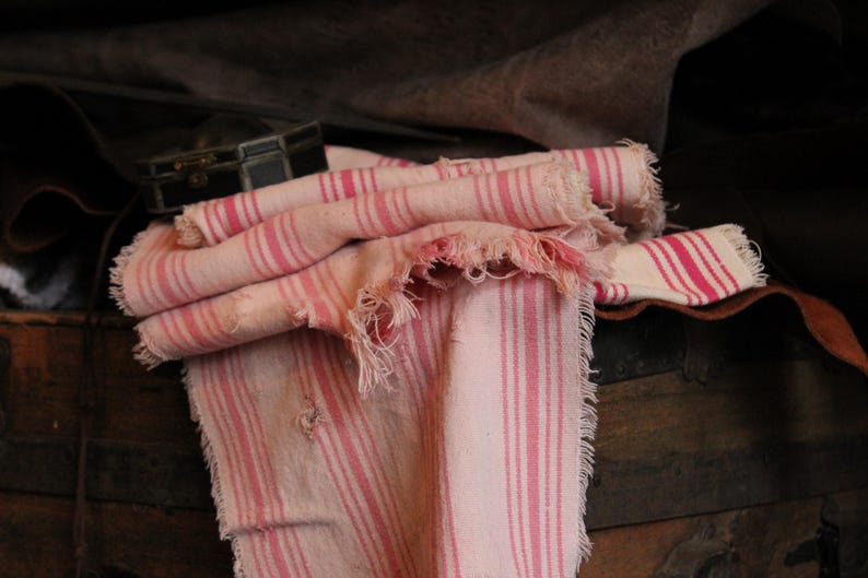 May include: A pink and white striped fabric with frayed edges. The fabric is folded and draped over a wooden surface.