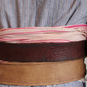 May include: A brown leather belt with a tan leather strap and a pink and white striped fabric belt underneath.