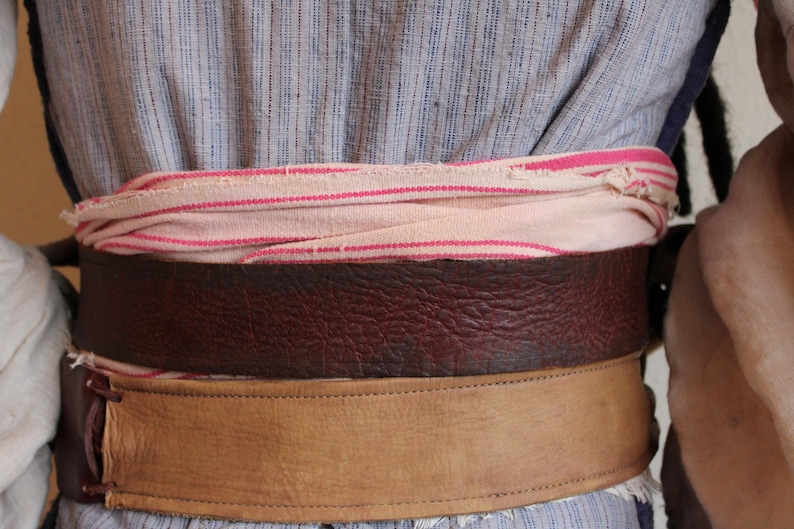 May include: A brown leather belt with a tan leather strap and a pink and white striped fabric belt underneath.