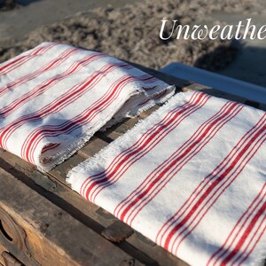 May include: Two white and red striped fabric napkins with frayed edges. The napkins are folded and placed on top of a wooden chest.