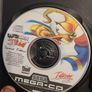 May include: Earthworm Jim Special Edition Sega Mega-CD game disc. The disc features a cartoon image of Earthworm Jim. The disc is in a black case. The disc has the Sega Mega-CD logo and the Interplay logo.