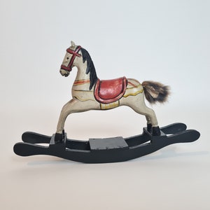 May include: A white and red painted wooden rocking horse with a black mane and tail. The horse is on a black wooden rocking base.