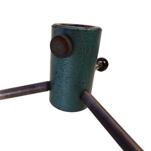 May include: A vintage Christmas tree stand with a teal-colored metal base and three dark metal legs. The stand has a dark brown knob and a black handle for securing the tree. The stand is designed to hold a Christmas tree upright.