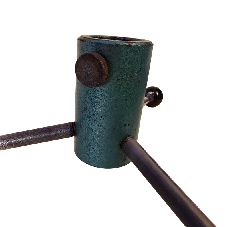 May include: A vintage Christmas tree stand with a teal-colored metal base and three dark metal legs. The stand has a dark brown knob and a black handle for securing the tree. The stand is designed to hold a Christmas tree upright.