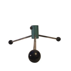 May include: A vintage Christmas tree stand with a teal green cylindrical base and three silver arms extending outwards. Each arm ends with a black sphere. A black sphere is also at the bottom of the stand.