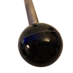 May include: Close-up of a black, glossy, spherical knob attached to a silver metal rod. The knob has a smooth, reflective surface with a horizontal seam. The rod is cylindrical and appears to be made of brushed metal.