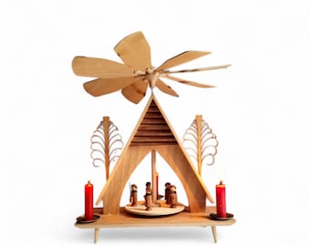 May include: A wooden Christmas pyramid featuring a natural light wood finish, a multi-bladed propeller at the top, and a central rotating platform with small carved figures. Two red candles stand on metal holders on the base, flanked by stylized trees.