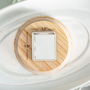 May include: A wooden coaster with a white rectangle in the center. The rectangle is 1.3 inches wide and 1.5 inches tall. The coaster is a great way to protect your furniture from hot drinks.