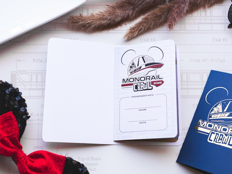 May include: A white passport-style booklet with a red and black logo that says "Monorail Crawl 2022". The logo features a cartoon image of a monorail. The booklet has a section for passenger information with the words "Name" and "Date" printed on it.