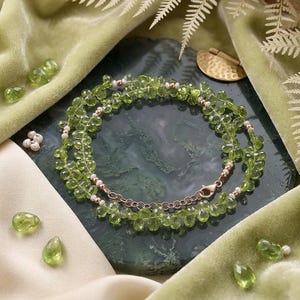 Peut inclure: Un collier composé de perles en forme de goutte en péridot vert clair facetté, agrémenté de petites perles blanches et de perles en or rose, terminé par un fermoir mousqueton en or rose et une chaînette de réglage.
