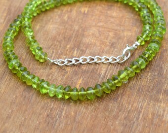 May include: A green peridot gemstone necklace with a silver chain clasp. The necklace is made of small, round beads and is approximately 18 inches long.