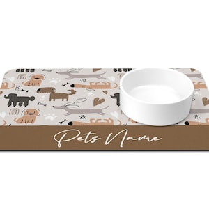 May include: A brown and white dog-themed pet bowl mat with a white ceramic bowl. The mat has a brown border with the text "Pets Name" in white.