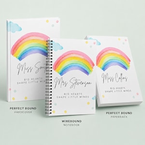 May include: Three notebooks featuring a watercolour rainbow design, light blue clouds, and colourful dots. The covers display the text "BIG HEARTS SHAPE LITTLE MINDS" and personalised names. One is a hardcover, one is wirebound, and one is a paperback.