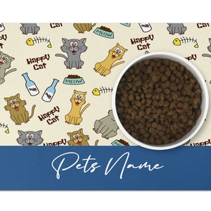 May include: A beige pet food mat with a cartoon cat design. The mat features a white bowl filled with brown kibble. The mat has the text "Happy Cat" and "Meow" repeated throughout. The mat has a blue border with the text "Pets Name" in white.