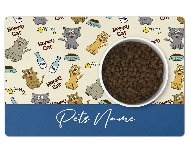 May include: A beige pet food mat with a cartoon cat design. The mat features a white bowl filled with brown kibble. The mat has the text "Happy Cat" and "Meow" repeated throughout. The mat has a blue border with the text "Pets Name" in white.