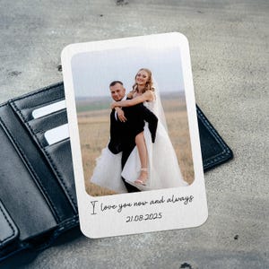 May include: A black leather wallet with a white card featuring a wedding photo of a couple. The card has the text "I love you now and always" and the date "21.08.2025". The photo shows a man carrying a woman in a field.