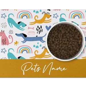 May include: White dog bowl with brown kibble on a white and yellow dog-themed placemat with the text "Pets Name" in white on a yellow background.