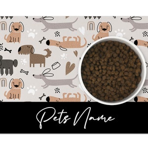 May include: A gray and white dog-themed pet bowl mat with a white bowl filled with brown dog food. The mat has a black border with the text "Pets Name" in white.