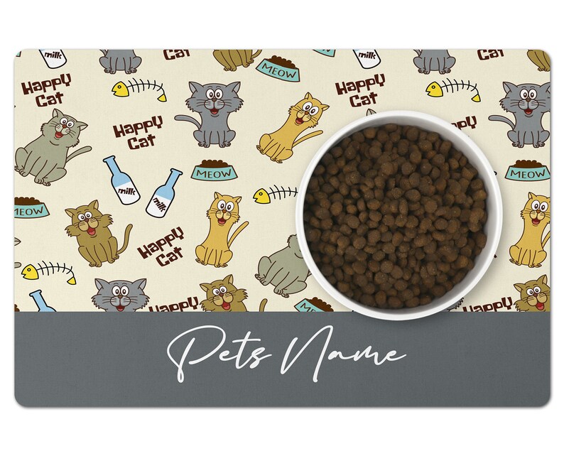 May include: A beige and gray cat-themed pet bowl mat with a white bowl filled with brown kibble. The mat has a repeating pattern of cats, fish bones, milk bottles, and the words "Happy Cat" and "Meow". The bottom of the mat is gray and has the text "Pets Name" written in white.