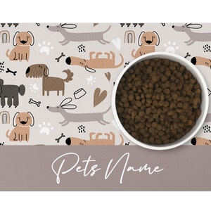 May include: A white dog bowl with brown dog food inside, sitting on a gray and white dog-themed placemat with the text "Pets Name".
