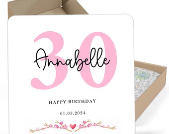 May include: A white card with pink 30 and the name Annabelle in black script. The text "Happy Birthday" and the date "01.03.2024" are below the name. A pink heart and pink flowers are at the bottom of the card.