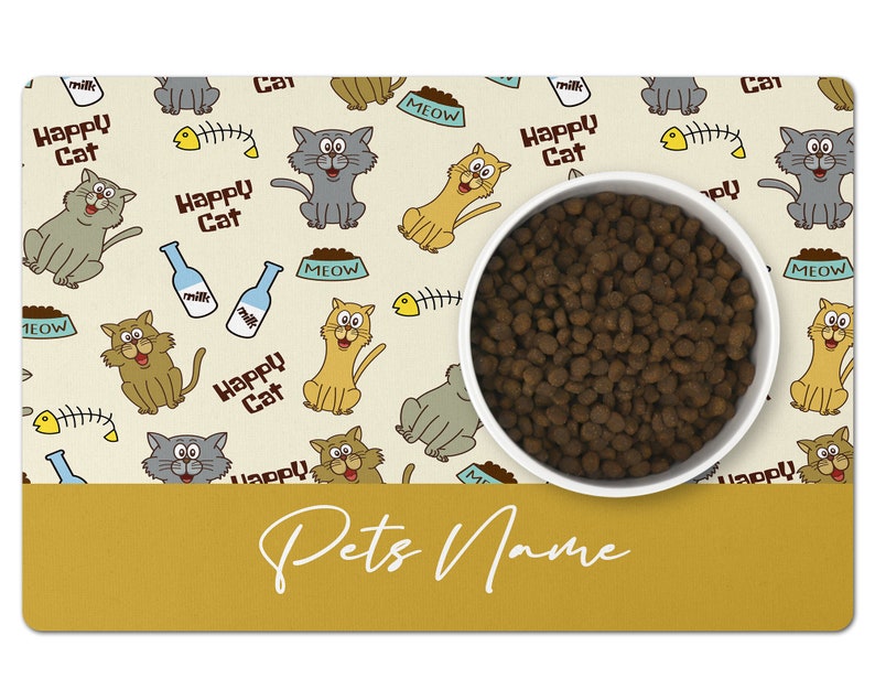 May include: A beige and yellow cat-themed pet bowl mat with a white bowl filled with brown kibble. The mat has a repeating pattern of cats, fish bones, milk bottles, and bowls that say "MEOW". The text "Happy Cat" is repeated throughout the mat. The bottom of the mat has a yellow bar with the text "Pets Name" in white.