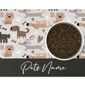May include: A white dog bowl with brown dog food inside, sitting on a gray and white dog-themed placemat with the text "Pets Name" at the bottom.