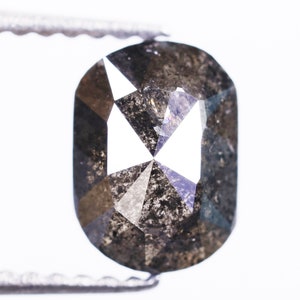 May include: A dark gray oval-shaped diamond with a faceted cut. The diamond has a lot of inclusions, which are small imperfections that give it a unique look.