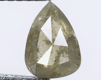 Puede incluir: Un diamante gris en forma de pera con un diseño facetado. El diamante se sostiene con unas pinzas.