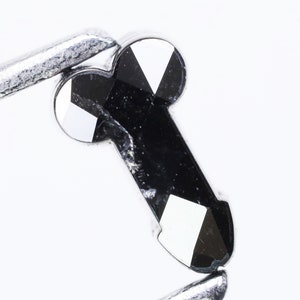 May include: A black diamond gemstone with a faceted cut. The diamond is held in a pair of tweezers.