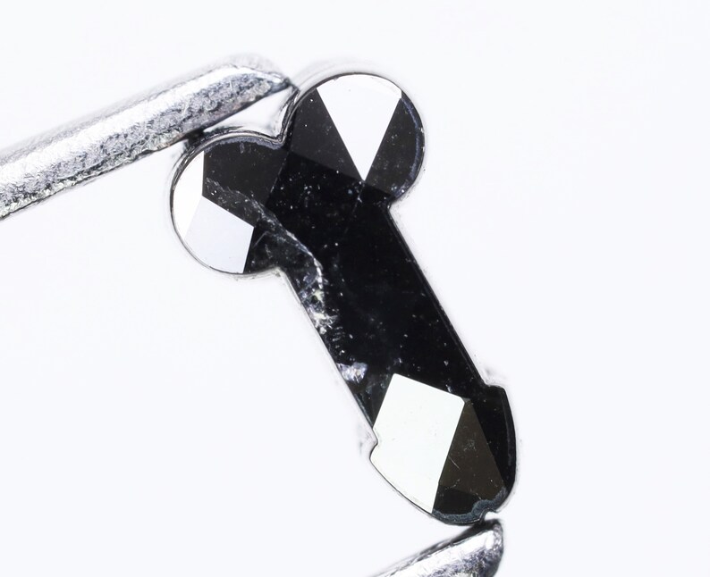 May include: A black diamond gemstone with a faceted cut. The diamond is held in a pair of tweezers.