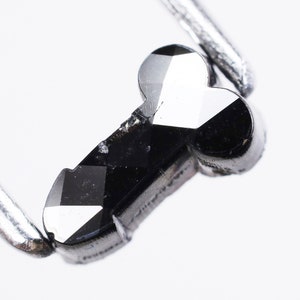 May include: A black diamond shaped like a key, held by a pair of tweezers.