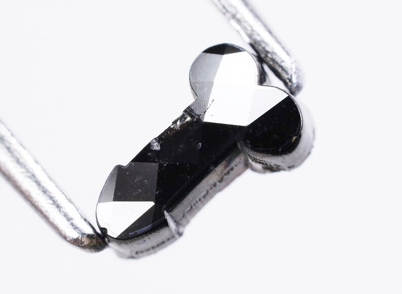 May include: A black diamond shaped like a key, held by a pair of tweezers.