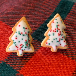 May include: Two white frosted Christmas tree-shaped cookies decorated with green and red sprinkles.