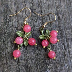 May include: A pair of dangle earrings with pink and green accents. The earrings feature a cluster of pink beads and green leaves.