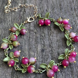 Può includere: Un braccialetto a catena dorata con foglie verdi e perline rosa e bianche. Il braccialetto ha una chiusura a moschettone.